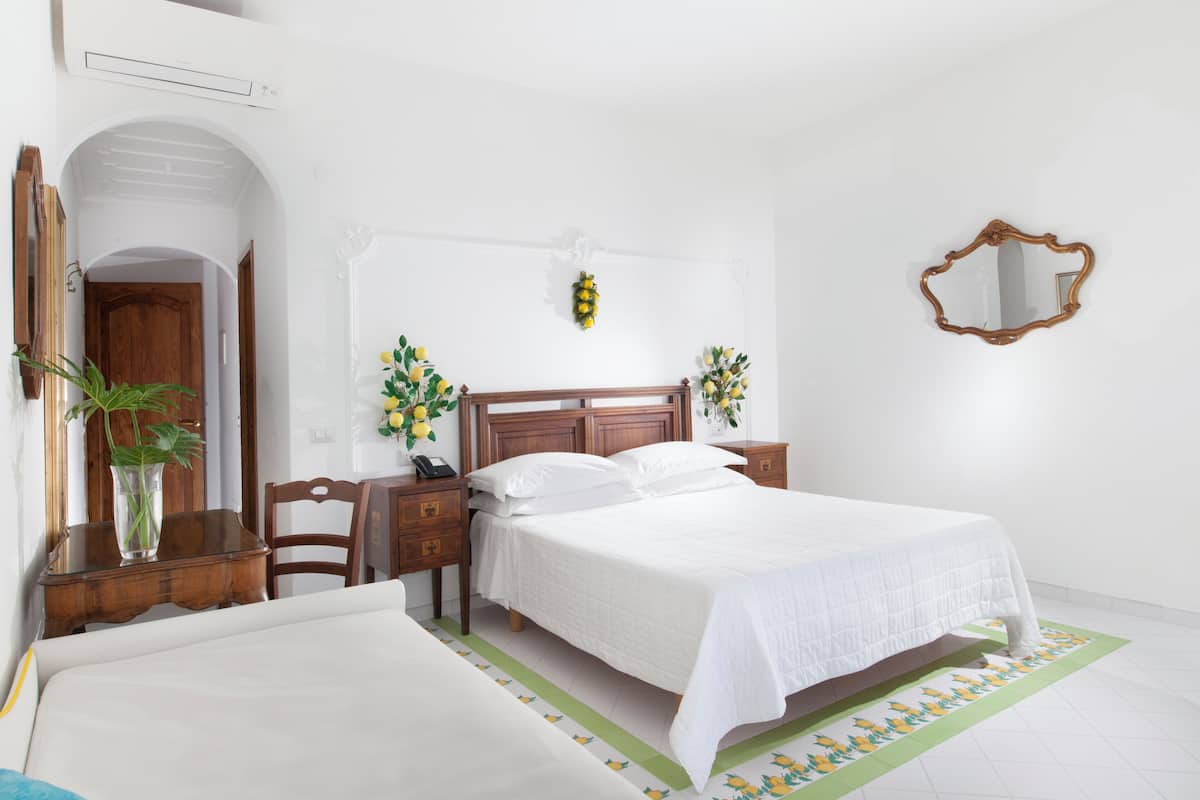 Un dormitorio ordenado con cama de madera, mesitas de noche, un espejo y un tapete floral verde.
