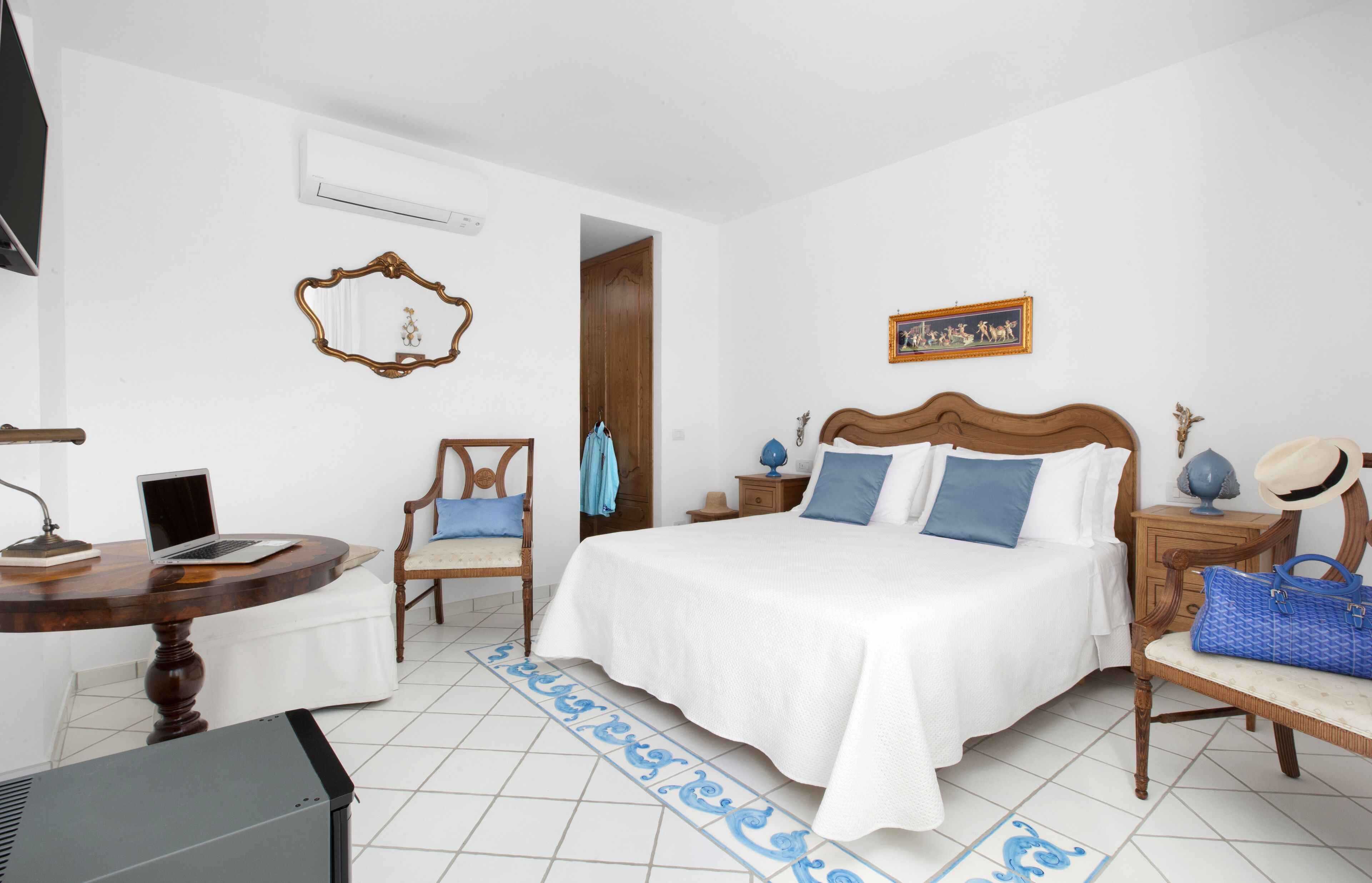 A bedroom with a bed, a chair, a desk with a laptop, a small table, and a wardrobe.