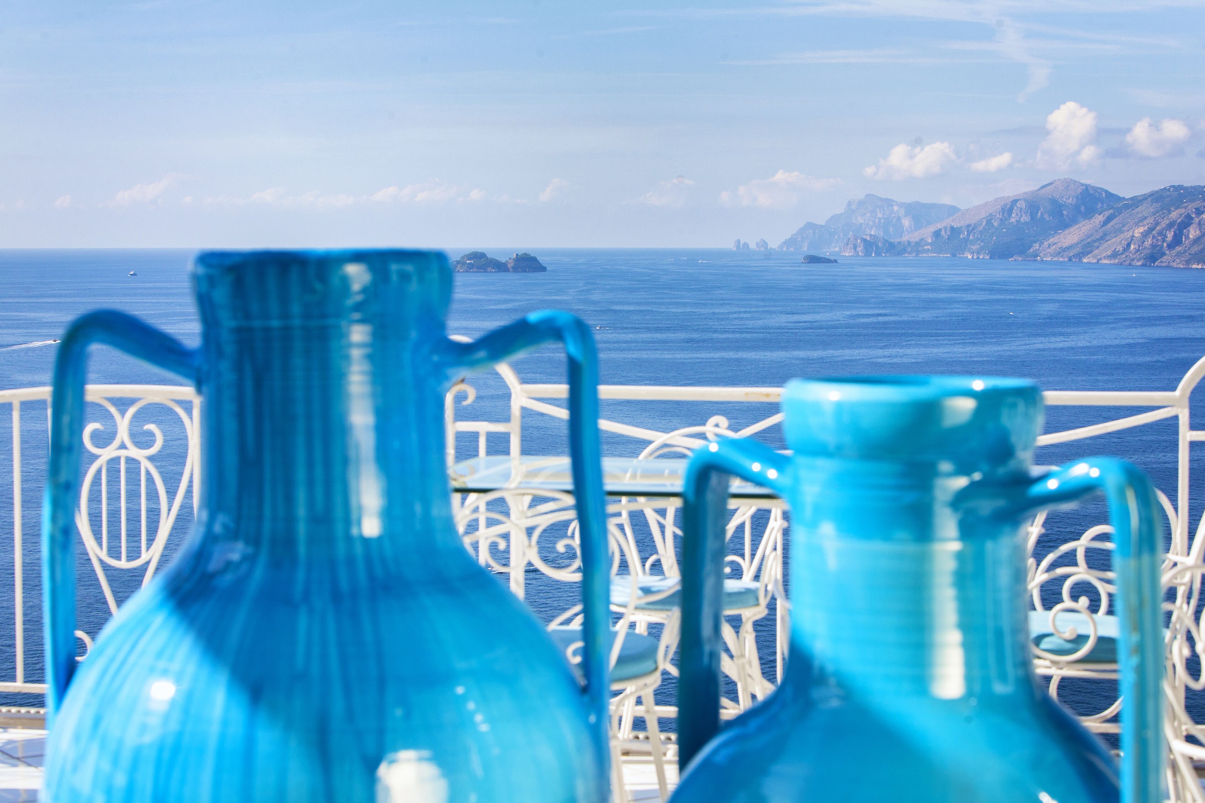 Un balcón con dos jarrones azules y vistas al mar y a las montañas.