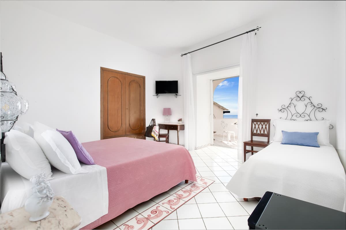 Un dormitorio con cama, escritorio, silla, televisor y vistas al exterior.