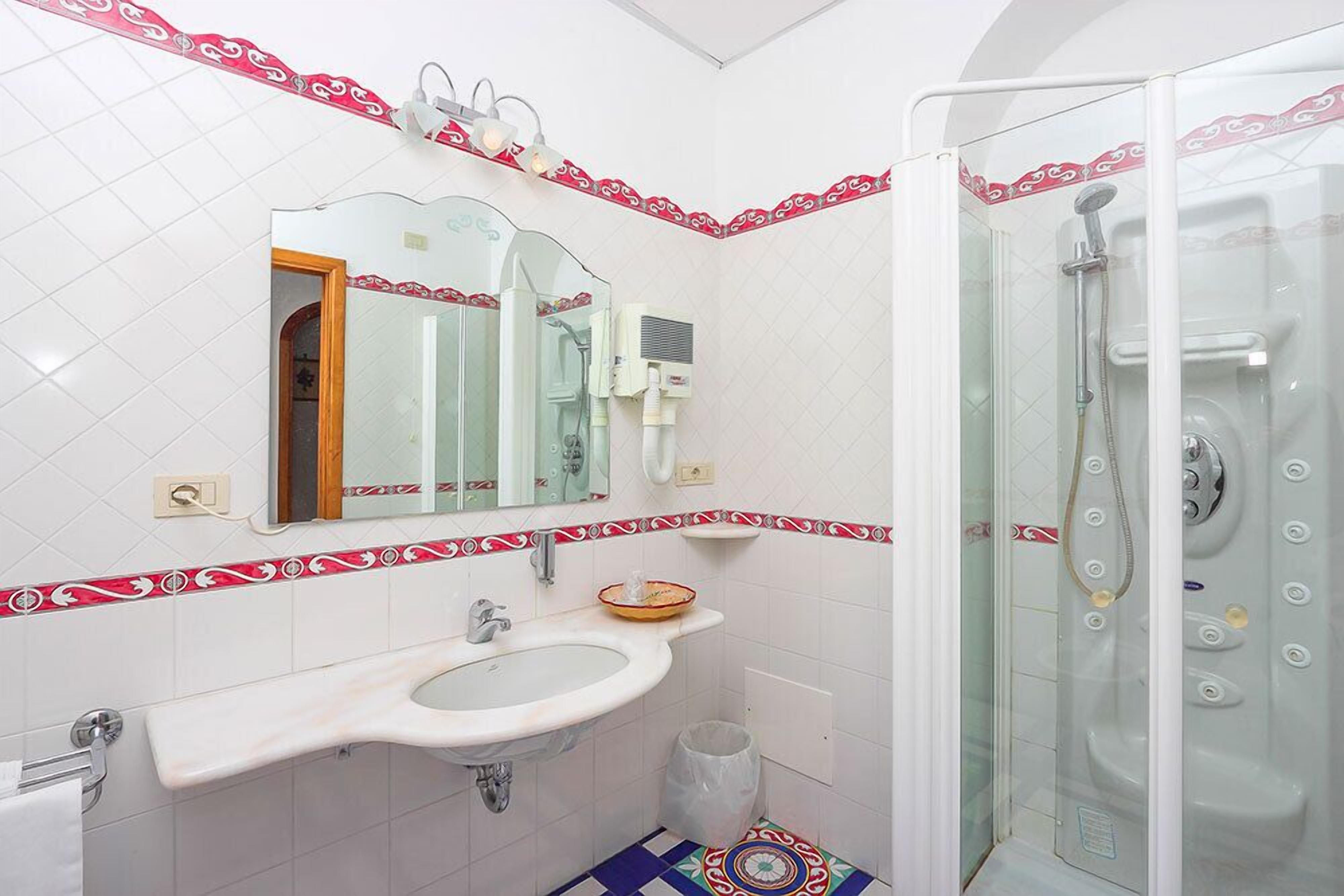 A bathroom with a white sink, a mirror, a shower, and a patterned tile border.