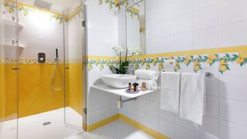 A bathroom with a glass-enclosed shower, a white sink with a mirror above it, and yellow and white tiles with a floral pattern.