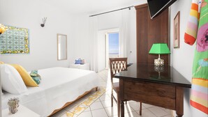 A bedroom with a bed, a desk, a chair, a TV, and a window with a view. - Hotel Smeraldo (Praiano)