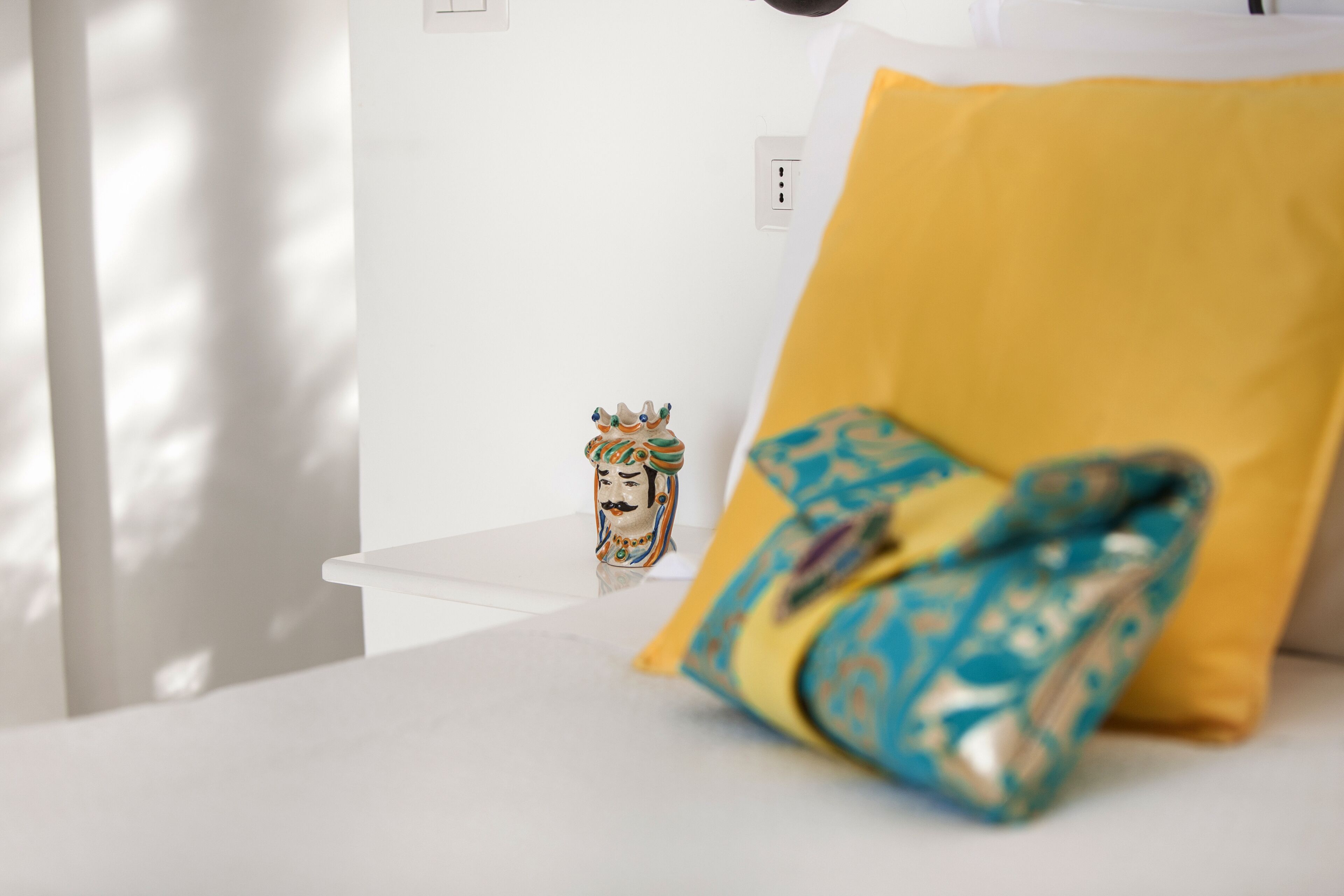 A white bedside table with a decorative object and a yellow pillow.