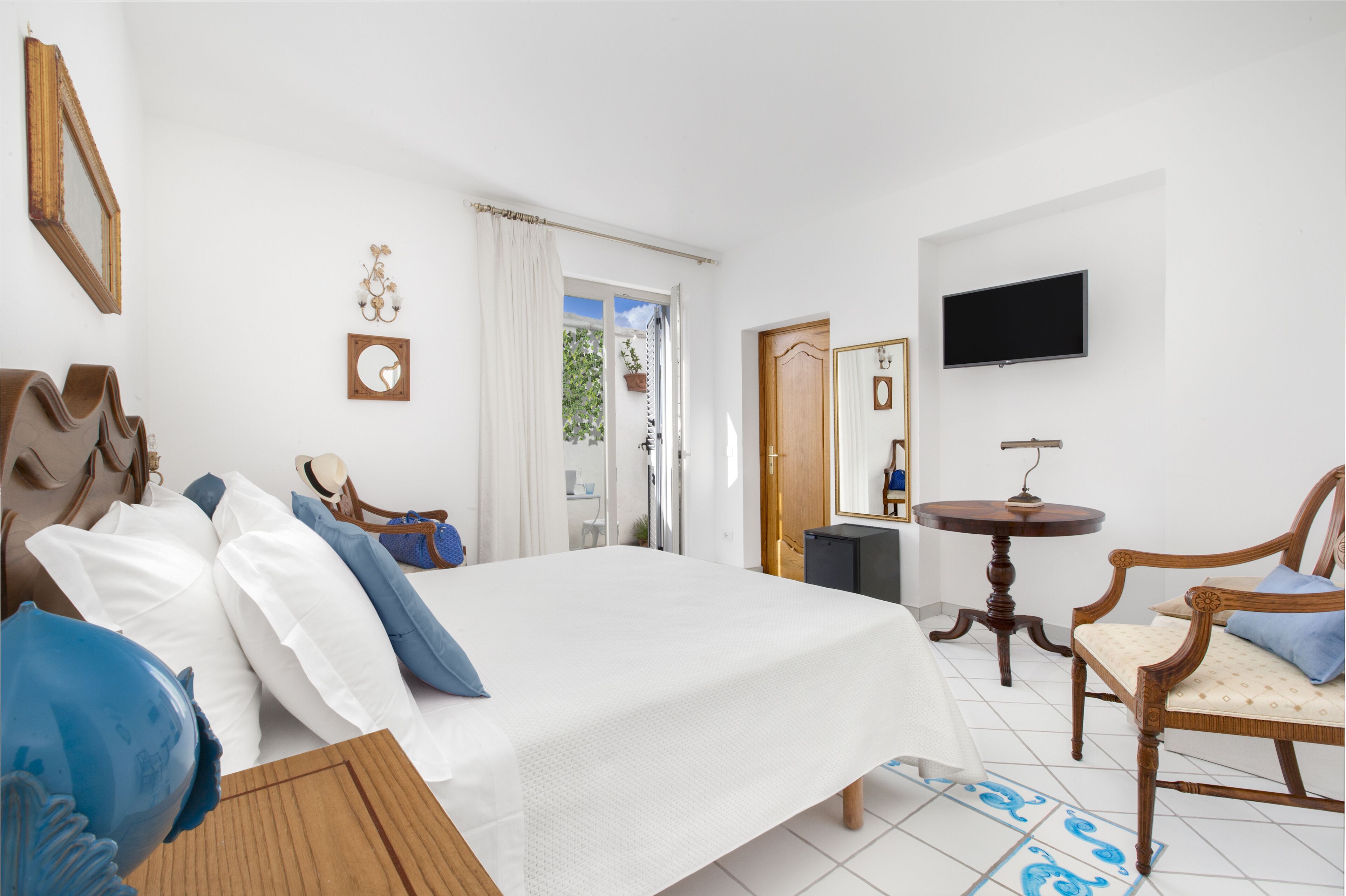Una camera d'albergo con un letto grande, una sedia di legno, un tavolino, una televisione e una finestra con tende.