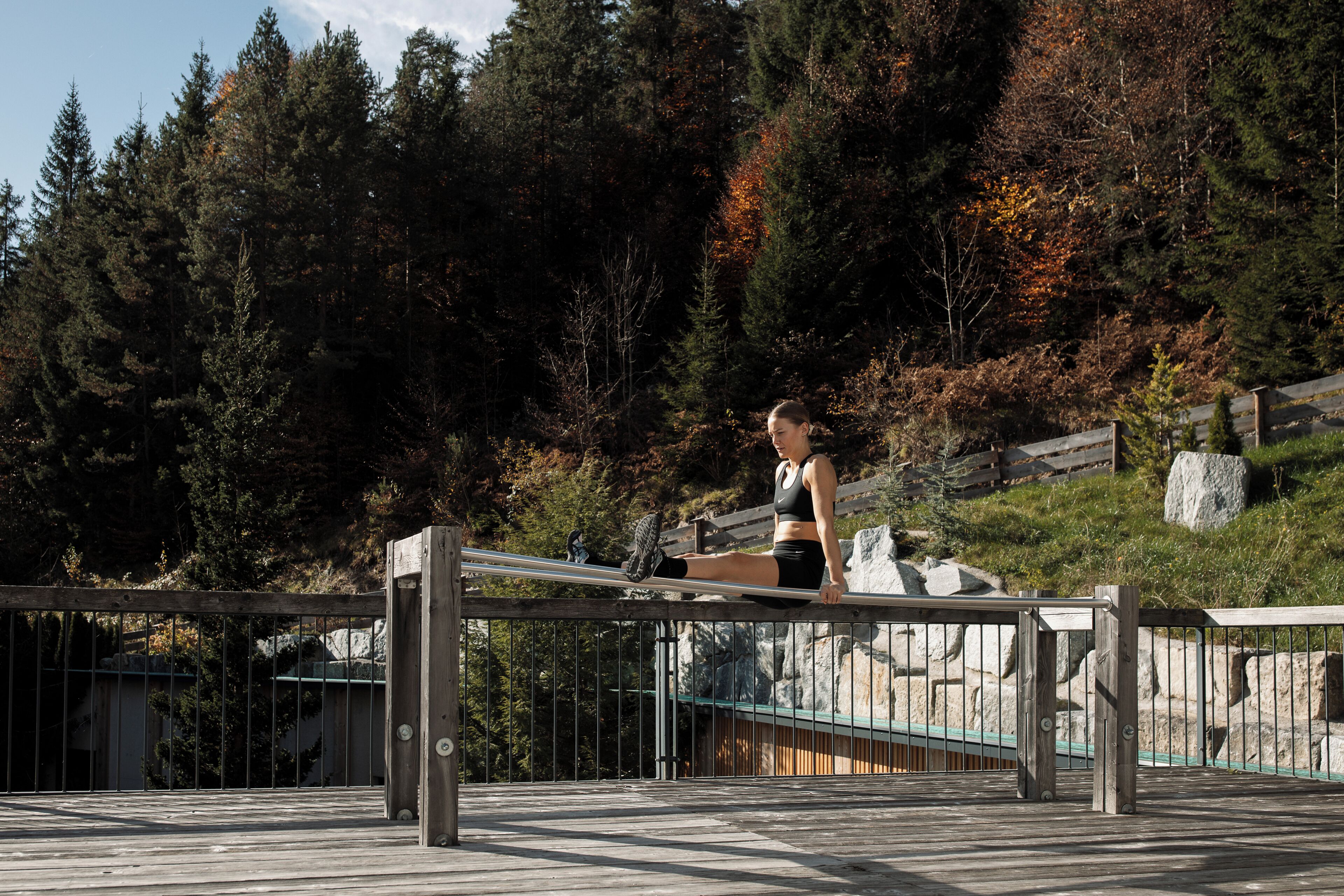 Eine Person trainiert auf einer Holzkonstruktion mit Metallstreben, umgeben von einem bewaldeten Gebiet mit Herbstlaub.