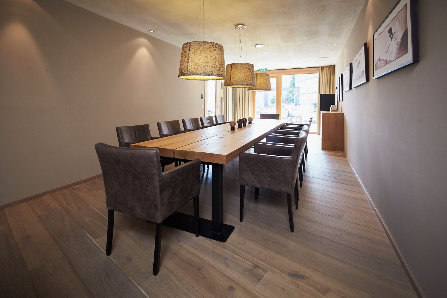 A long wooden dining table with matching chairs, a modern pendant light fixture, and framed pictures on the wall.