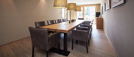 A long wooden dining table with matching chairs, a modern pendant light fixture, and framed pictures on the wall.