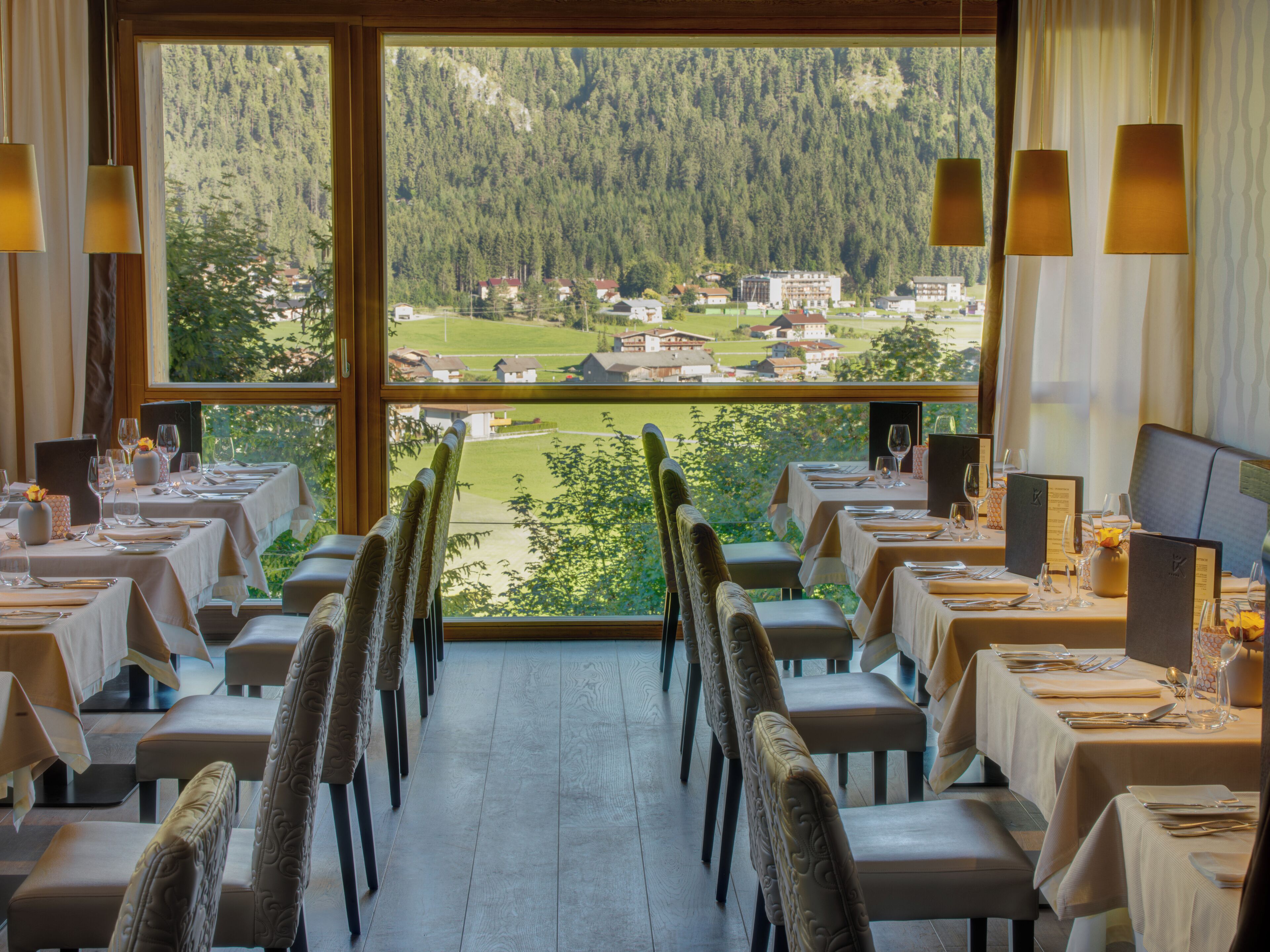 A restaurant with tables set for dining, a view of a forested area, and a dining area with chairs and tables.