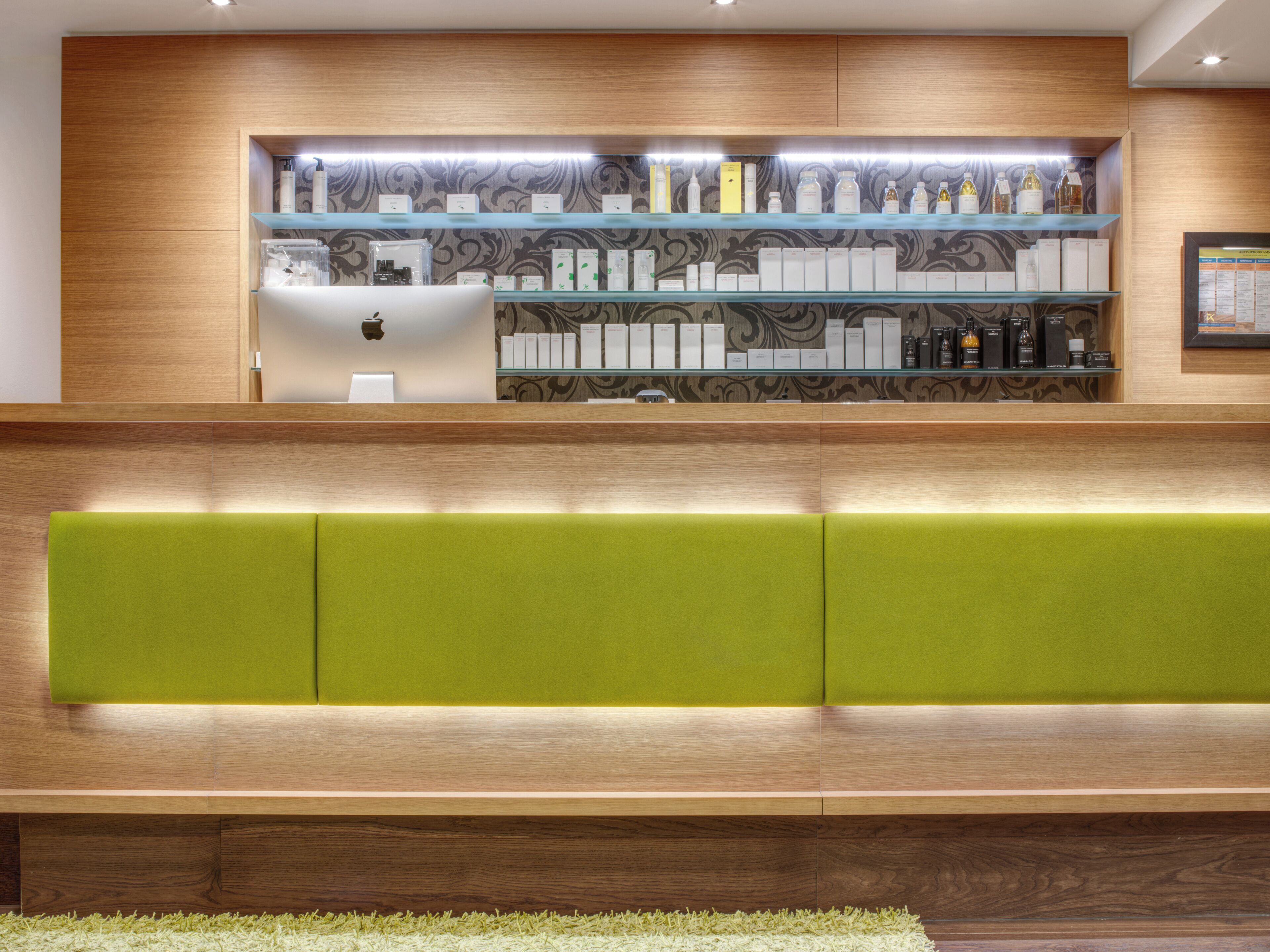 A reception area with a wooden reception desk, a green cushioned seating area, and shelves displaying various products.