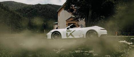 Un coche blanco aparcado en un campo verde con una casa al fondo.