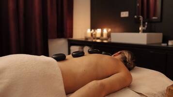 A person receiving a hot stone massage in a dimly lit room with a sink and candles in the background.