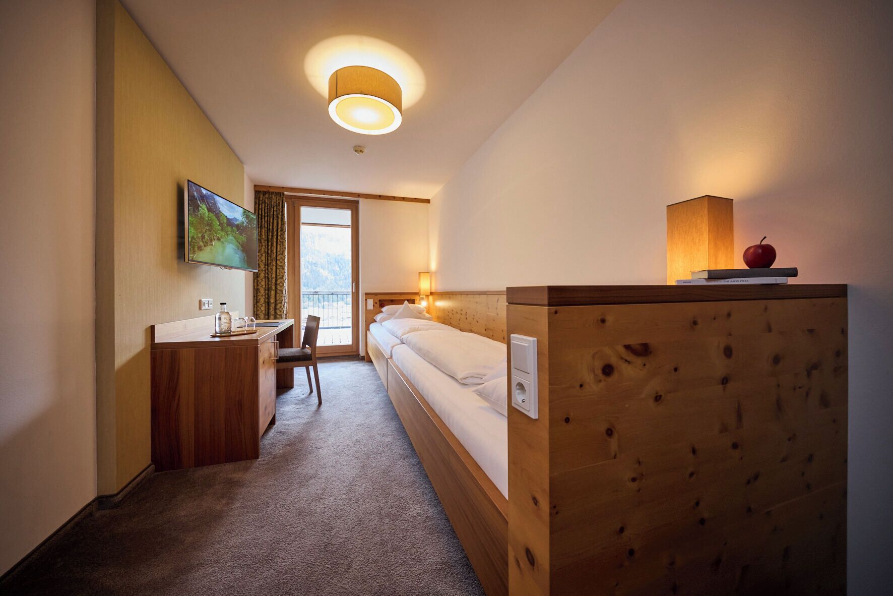 A hotel room with a bed, a desk, a chair, a TV, and a wooden partition.