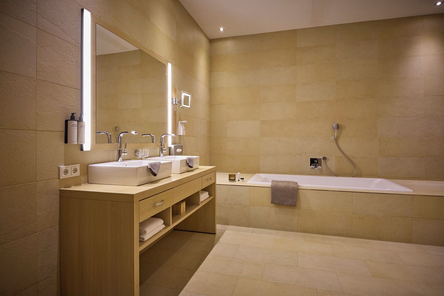 A modern bathroom with a double sink vanity, a large bathtub, and a wall-mounted mirror.
