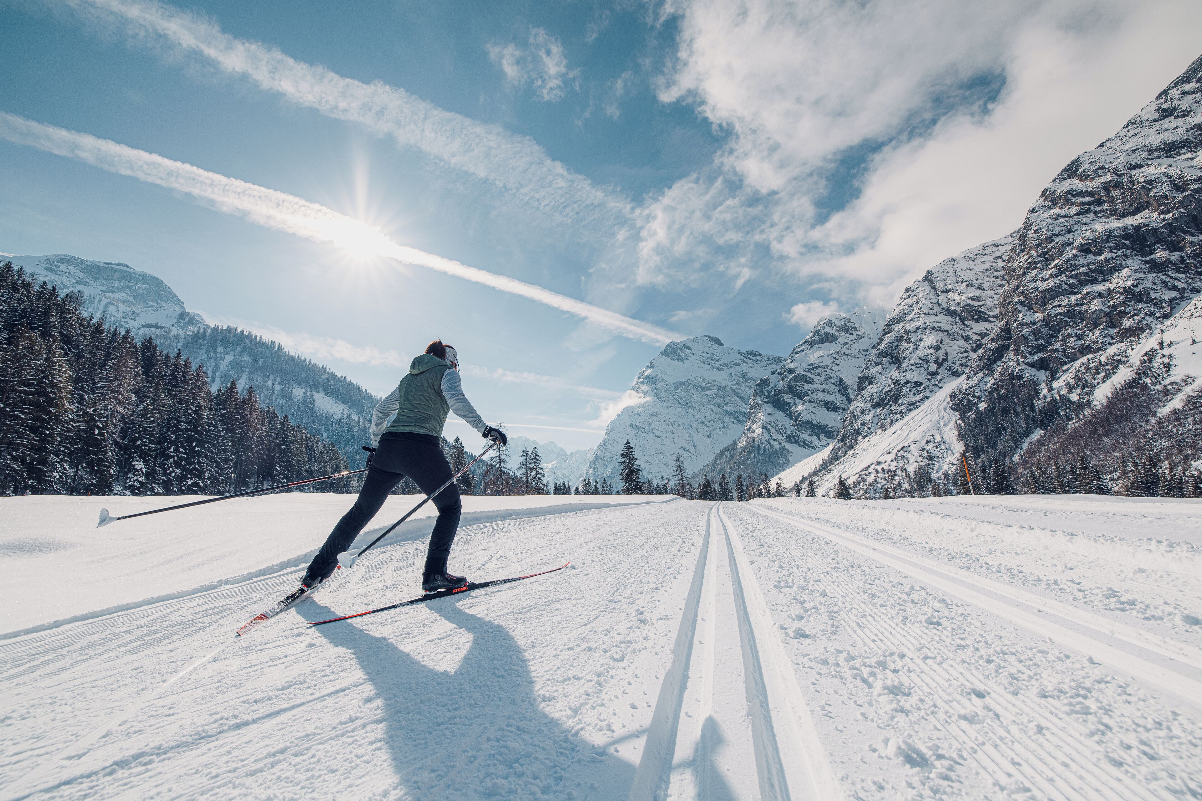 A person skiing on a snow-covered path with mountains in the background.