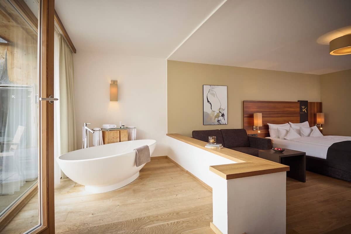 Una habitación de hotel moderna con una bañera grande, un sofá, una cama y un mostrador de madera.