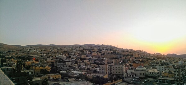 A cityscape with a prominent mosque and a dome, surrounded by residential buildings and a hilly backdrop during sunset.