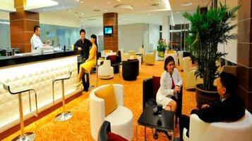 A modern hotel lobby with a reception desk, seating area, and a large plant.