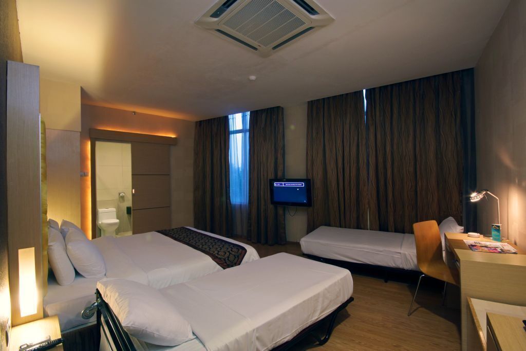 A hotel room with two beds, a desk, a chair, a TV, and a bathroom visible through an open door.