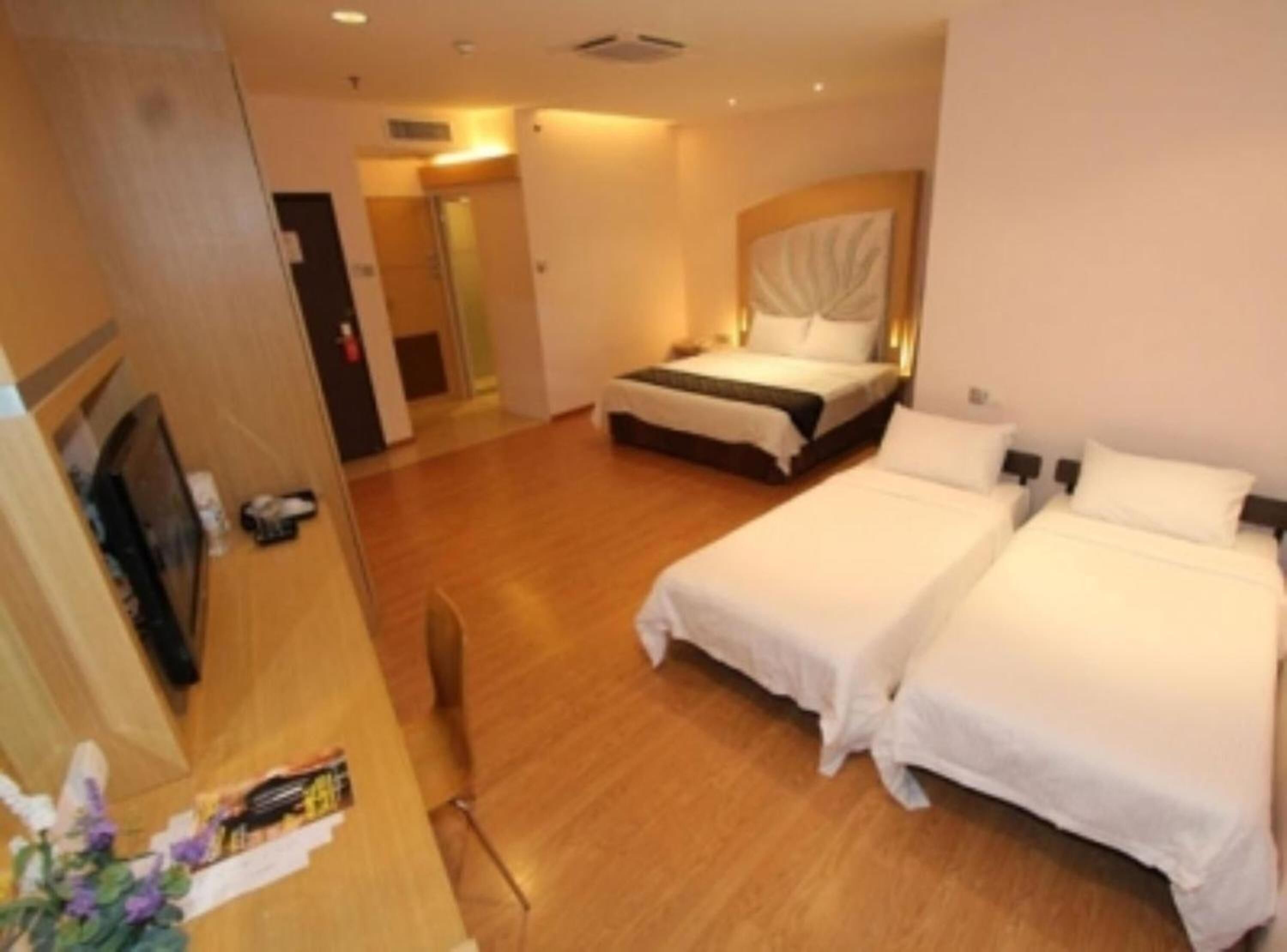 A hotel room with two beds, a television, and a wooden floor.