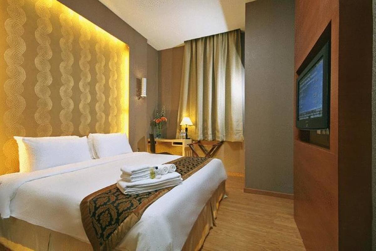 A hotel room with a large bed, a desk, a chair, a lamp, and a TV on the wall.