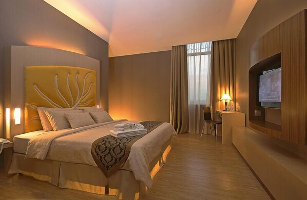 Quarto de hotel com uma cama grande, televisão na parede, mesa com cadeira e janela com cortinas.