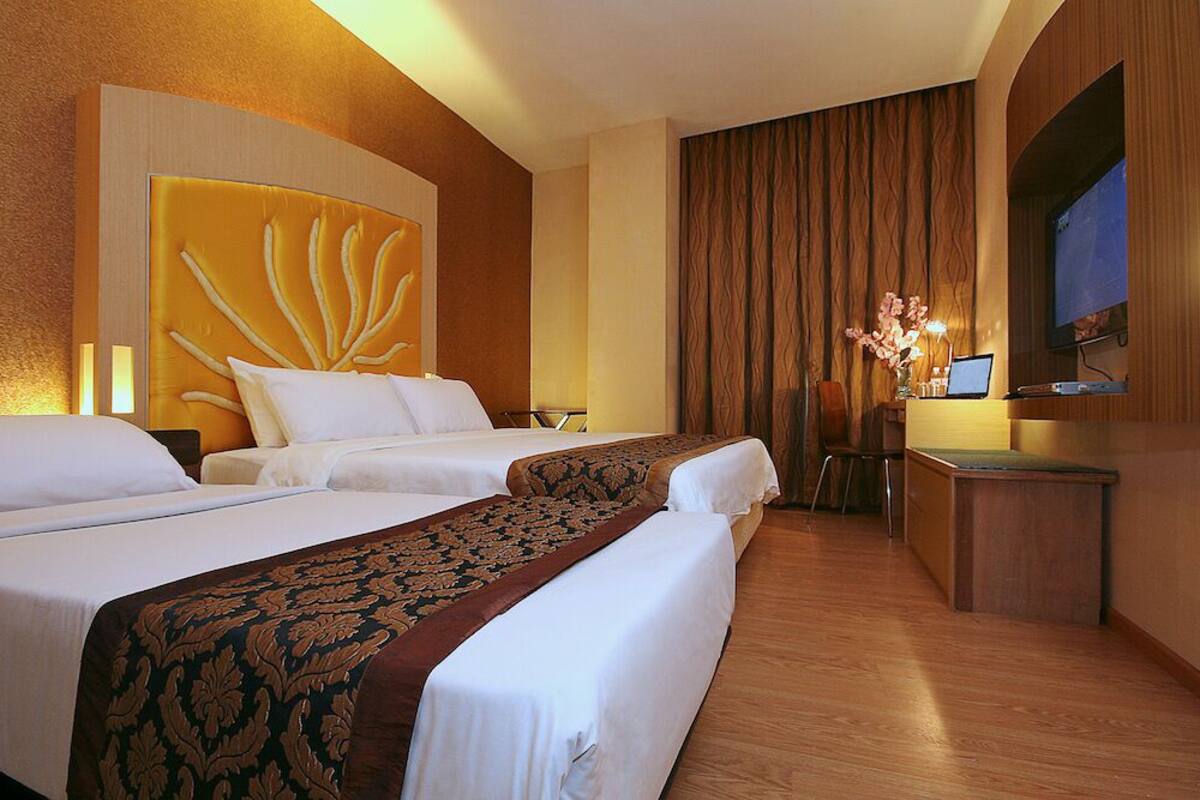 A hotel room with two beds, a desk with a computer, and a large window with curtains.