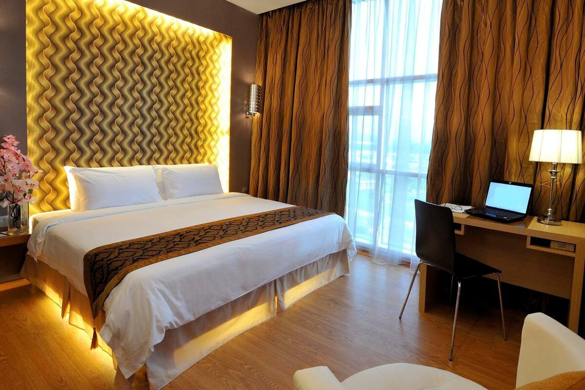 A hotel room with a large bed, a desk with a laptop, a chair, and a TV.