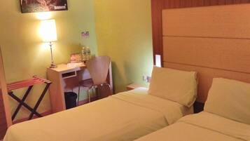 A hotel room with two beds, a desk with a chair, a lamp, and a small table with a bottle and a menu.