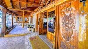 Un edificio de madera con zócalo de piedra, ventanas amplias y una campana en la pared.
