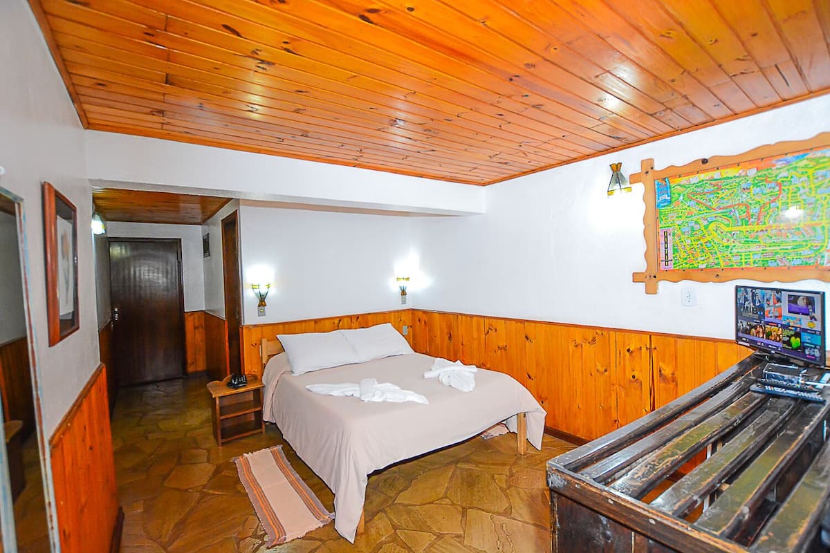 Habitación de hotel con techo de madera, cama con ropa de cama blanca, suelo de piedra, banco de madera, televisor montado en la pared y un mapa en la pared.