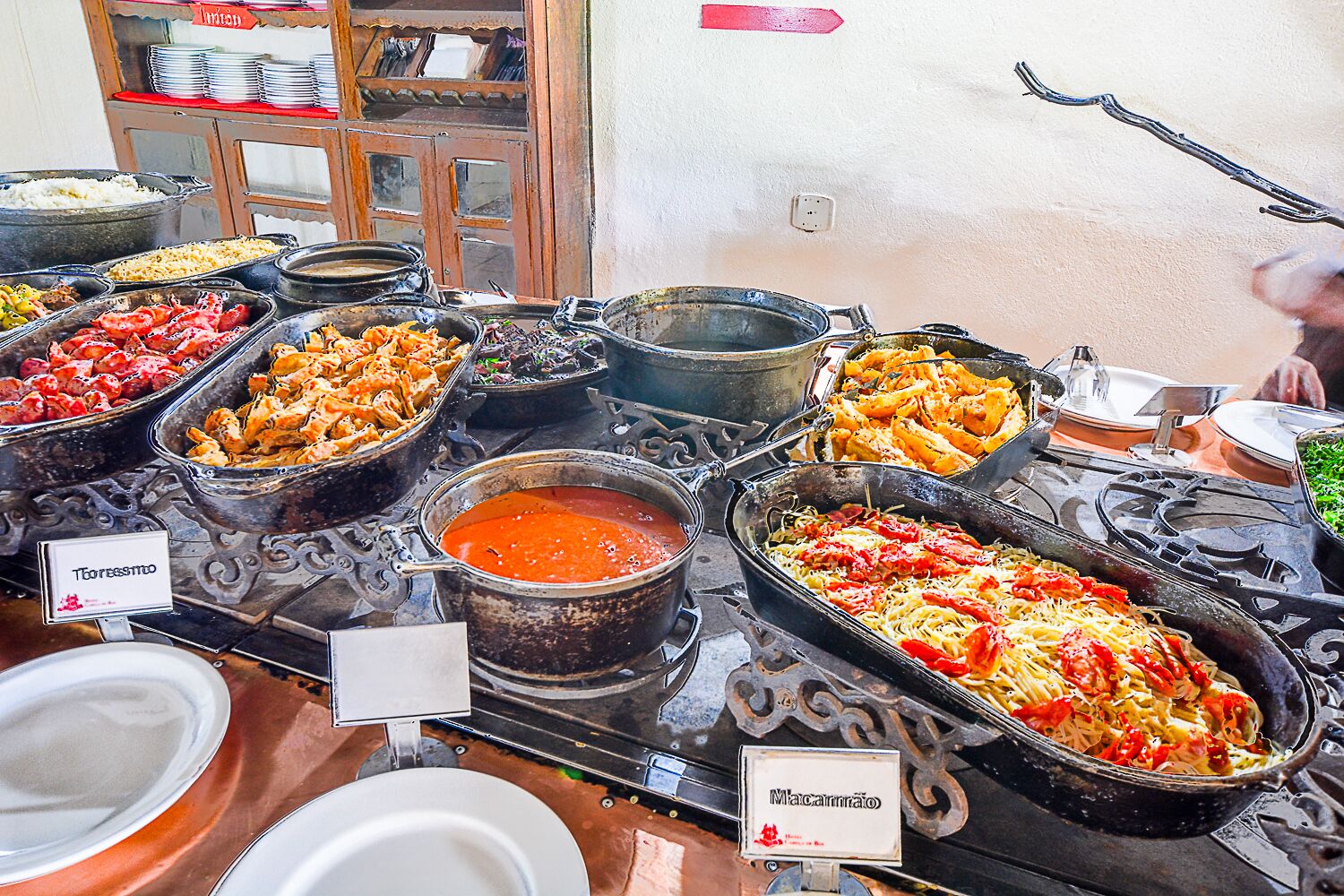 Buffet com diversos pratos identificados, incluindo 'Teofessino' e 'Macarrão'.