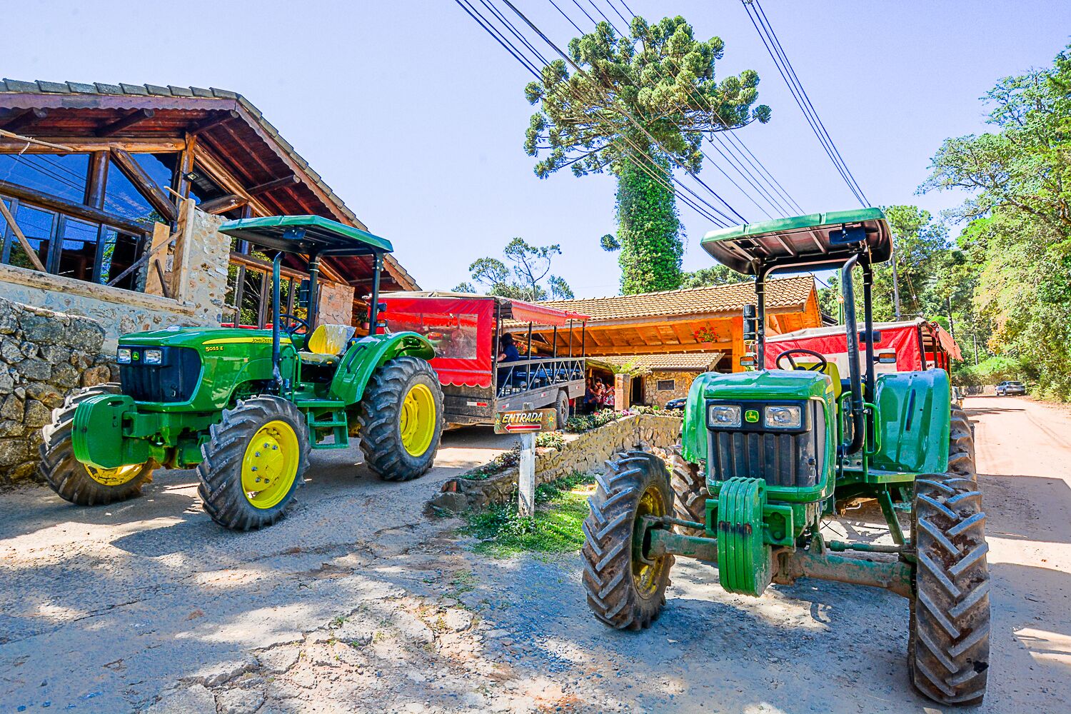 Dois tratores verdes estacionados em frente a um edifício rústico com parede de pedra e telhado de madeira.