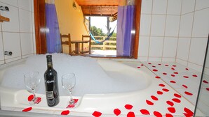 Una bañera llena de burbujas, dos vasos y una botella de vino, con pétalos de rosa roja esparcidos alrededor.
