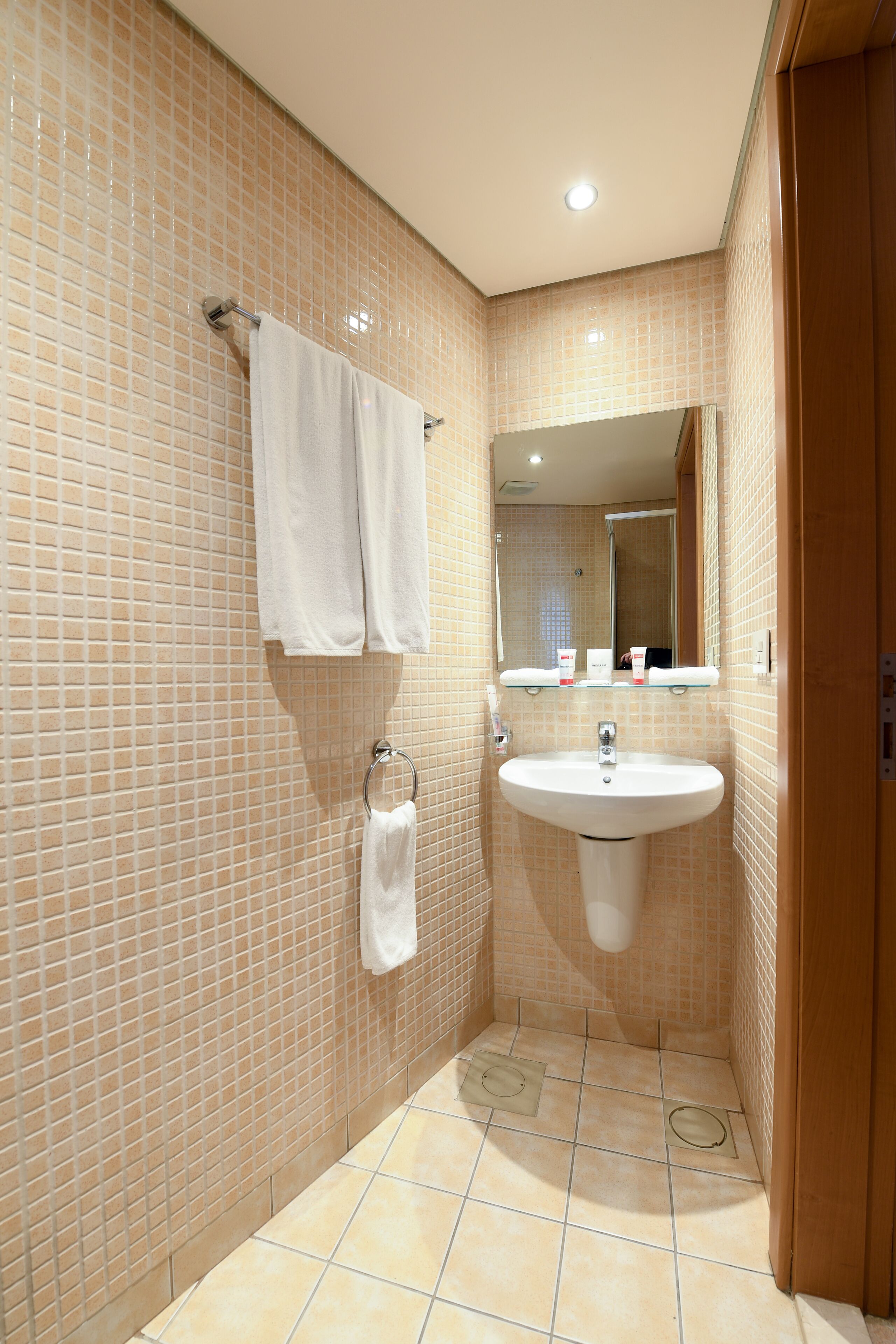 Un baño con paredes de azulejos color crema, un lavamanos blanco y un espejo encima.