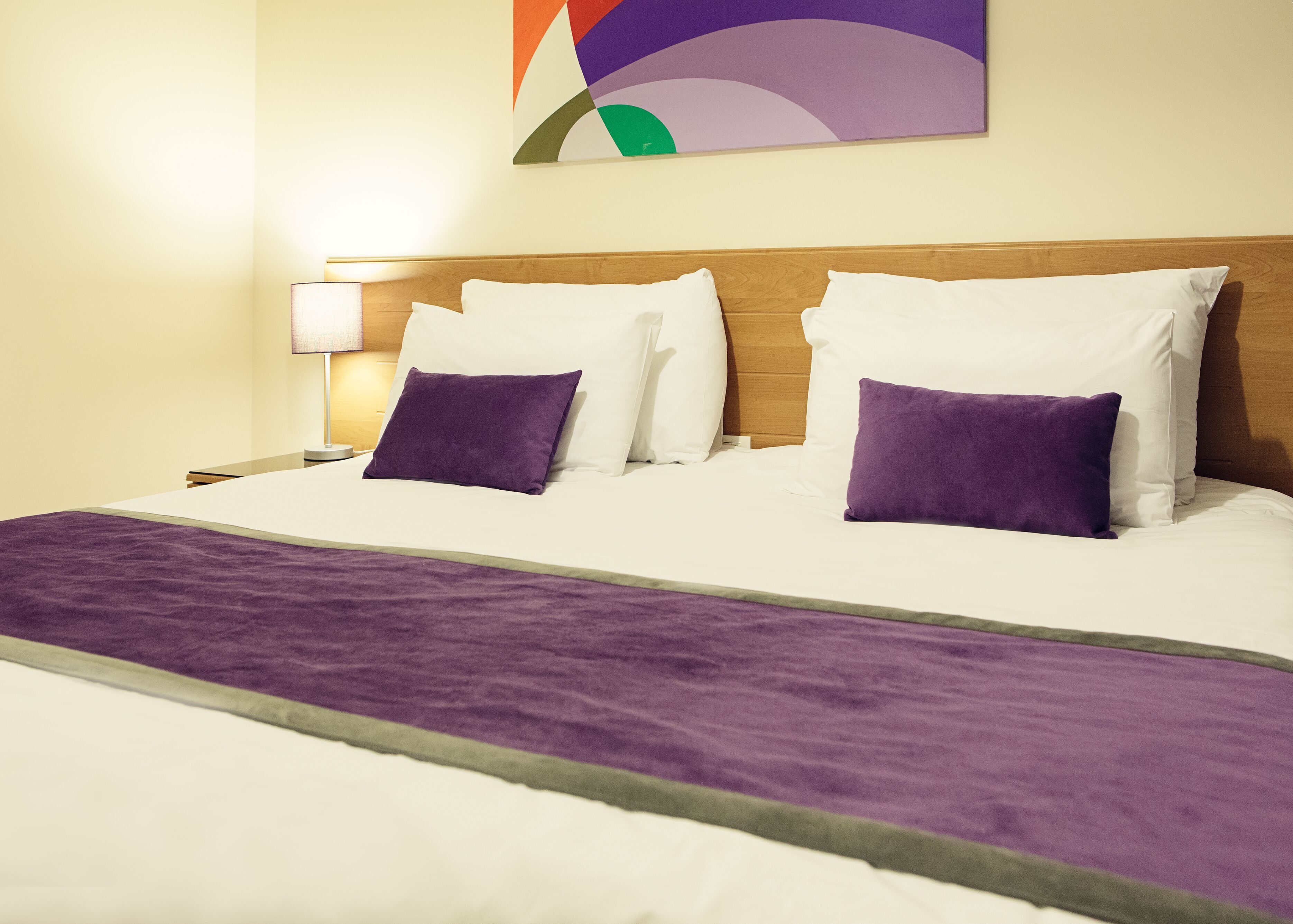 A hotel room with a large bed, a wooden headboard, and a purple throw blanket.