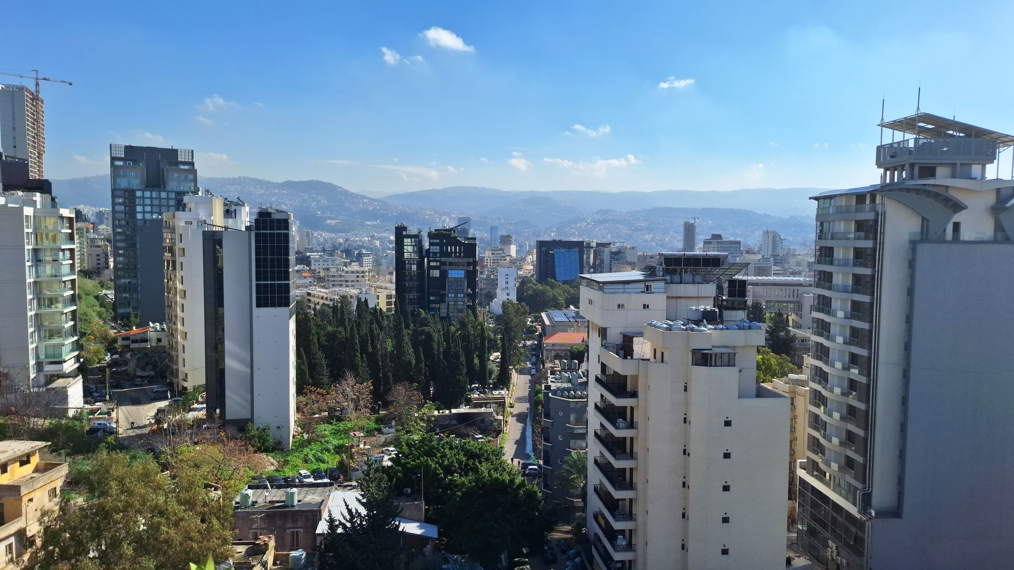 A cityscape with modern high-rise buildings, a clear sky, and distant mountains.