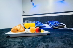 A breakfast tray with croissant, orange juice, and fruit on a marble table in a hotel room with a bed and blue-striped pillows. - Hotel LB Villa De Cuenca (Cuenca)