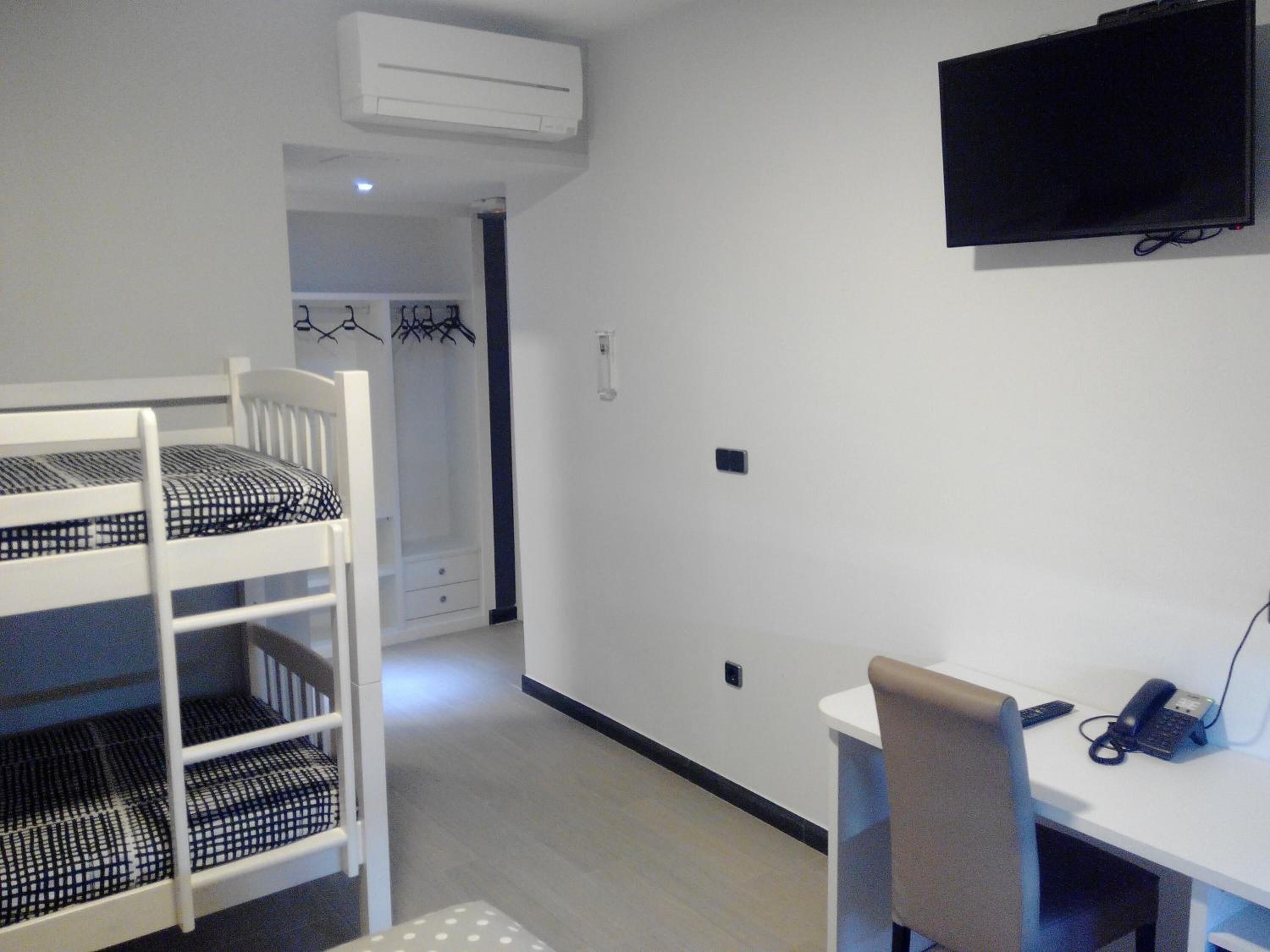 A room with bunk beds, a desk, a chair, a flat-screen TV, and a telephone.