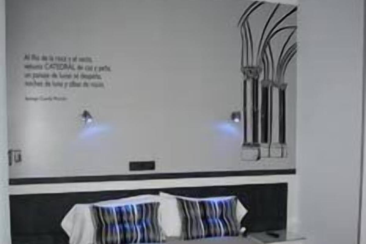 Un dormitorio moderno con una cama grande, una mesita de noche y un aplique en la pared.