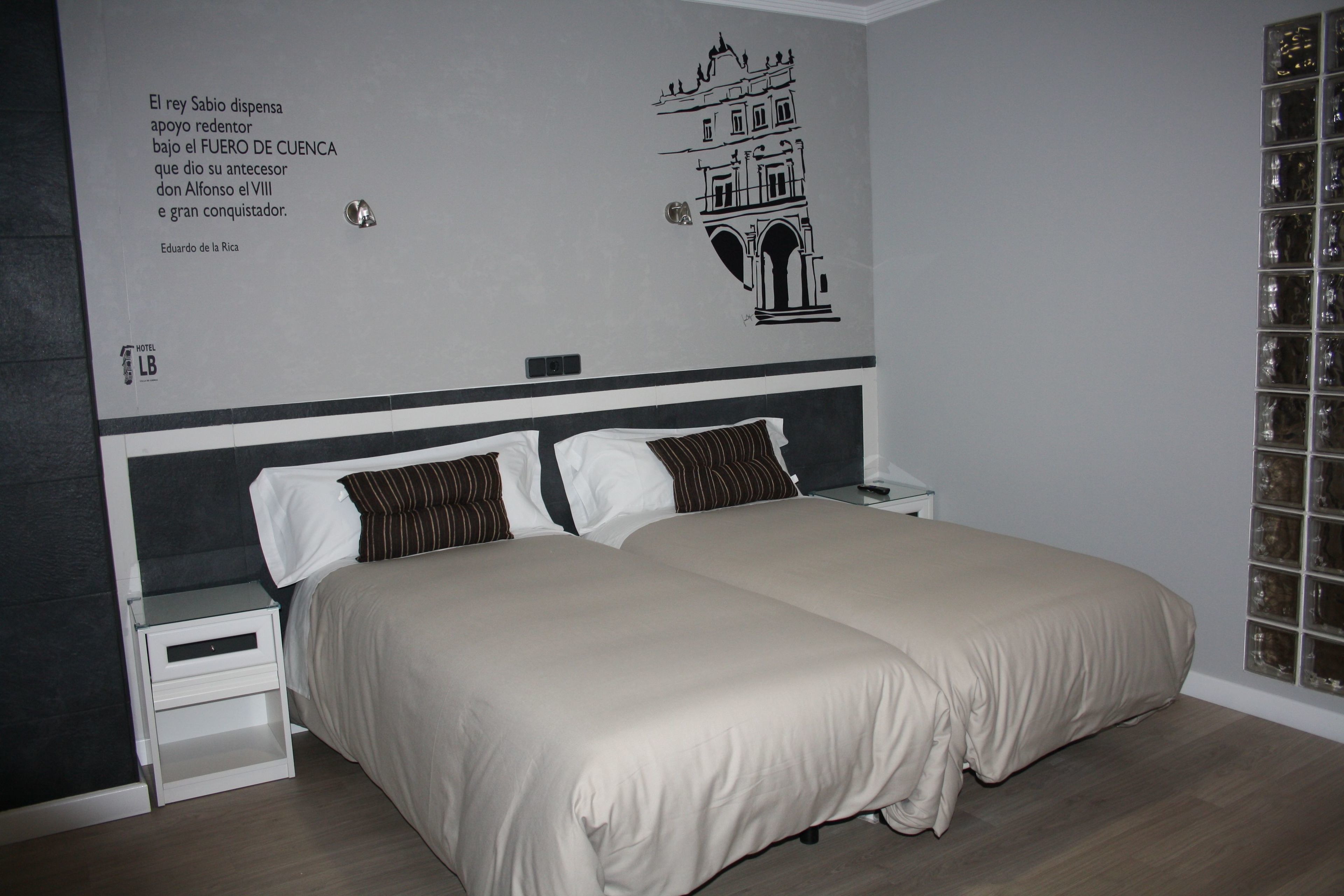 Habitación de hotel con una cama grande, dos almohadas, una mesita de noche y una pared con un mural en blanco y negro.