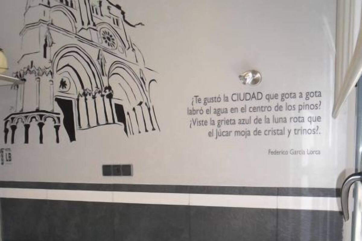Habitación de hotel con cama, mesita de noche y un mural en blanco y negro con una cita en español.