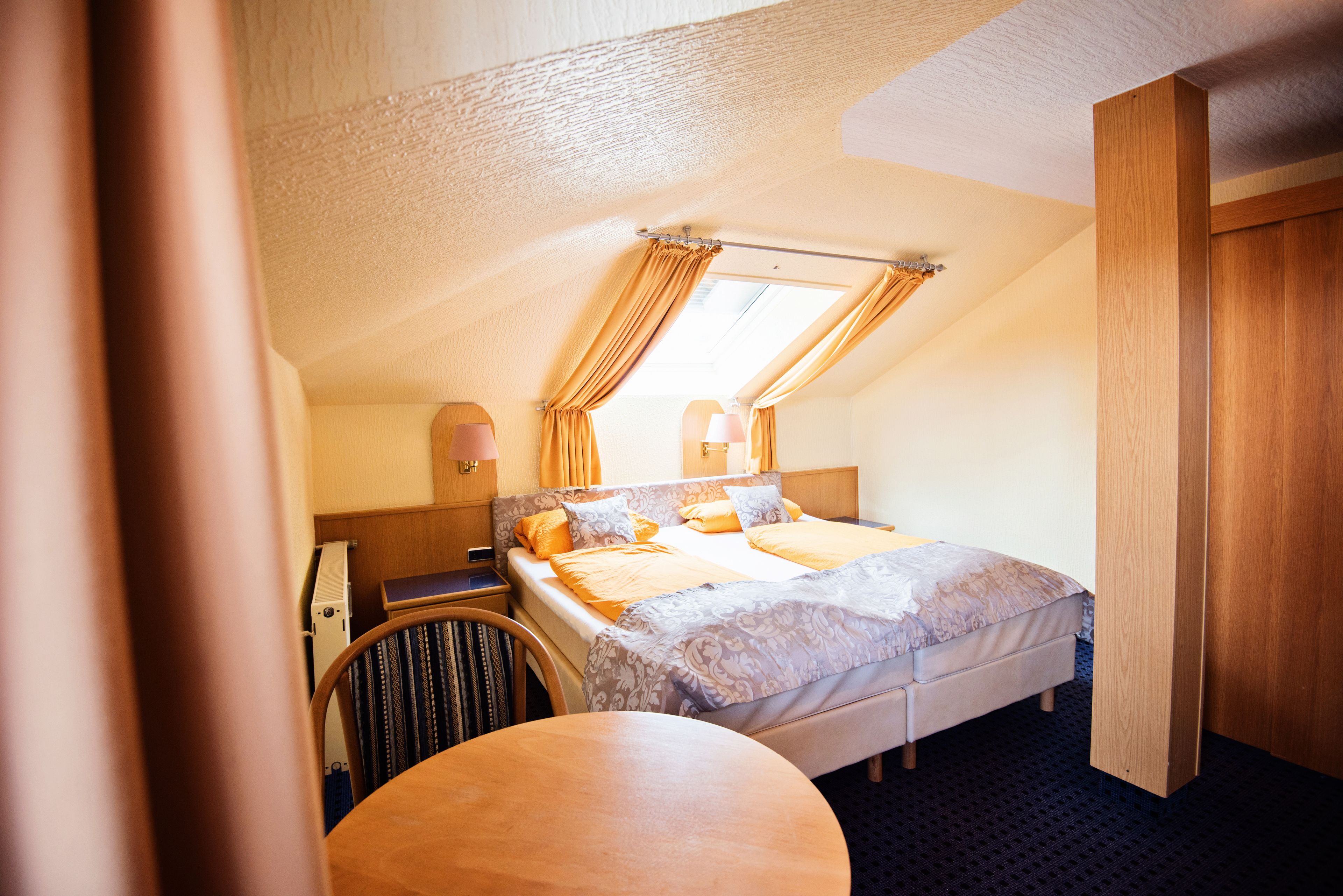 Una habitación de hotel con una cama, una mesa redonda, una silla y una ventana con cortinas.