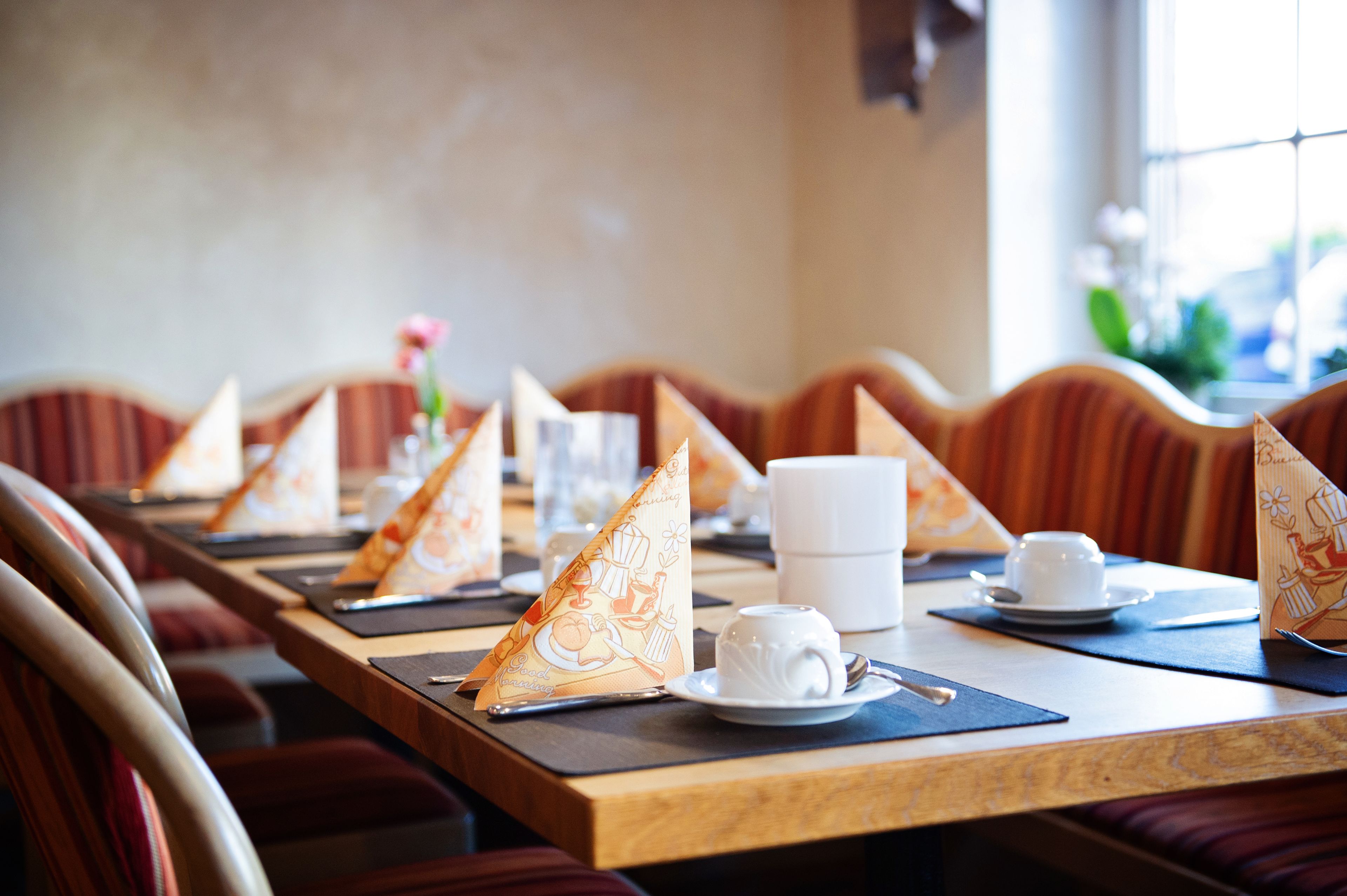 A restaurant table set with a white cup, saucer, spoon, napkin, and a menu.