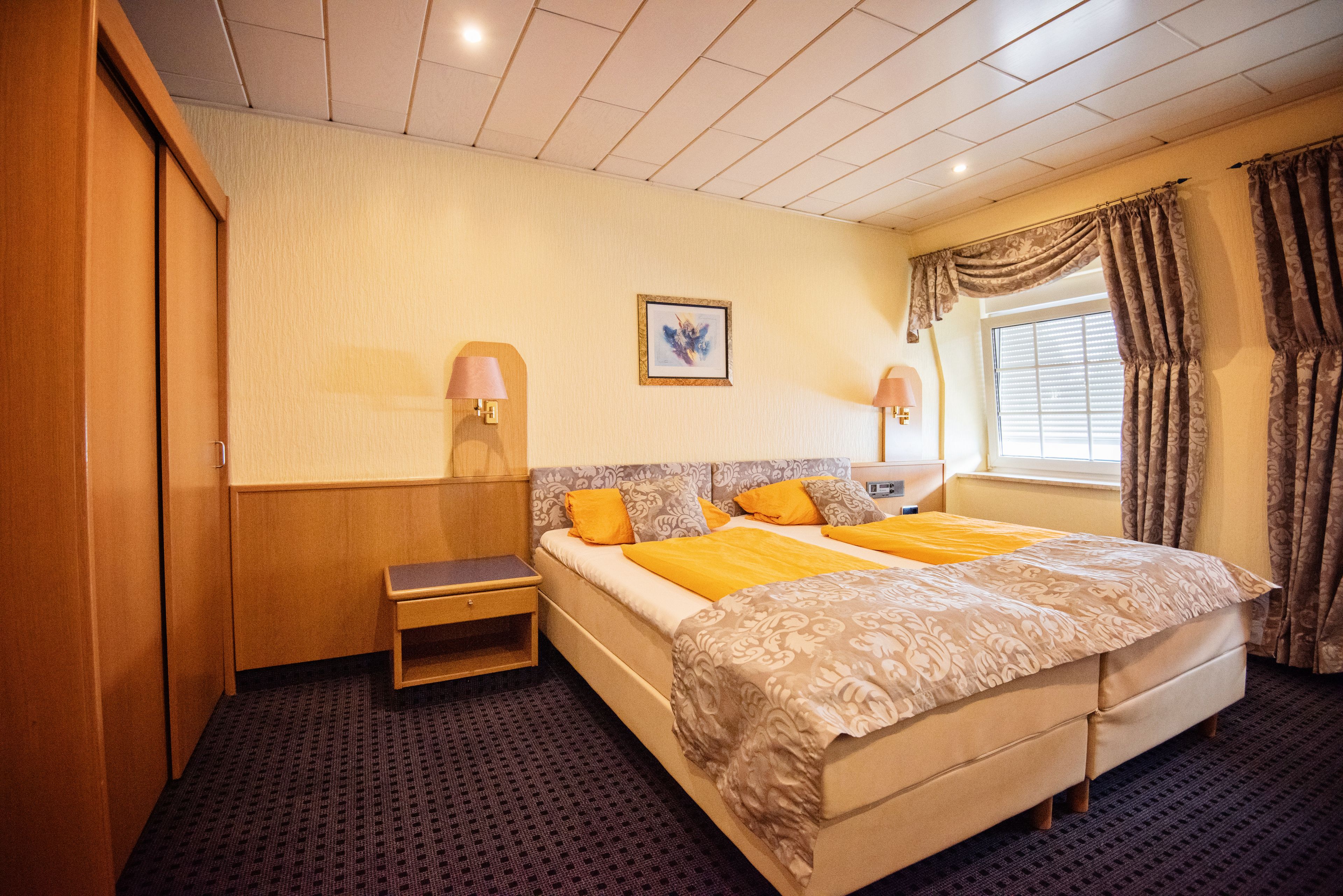 A hotel room with a large bed, bedside tables, a wardrobe, and a window with curtains.