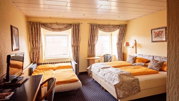 A hotel room with two beds, a desk, a chair, a table, and a window with curtains. - Hotel Heideparadies (Soltau)
