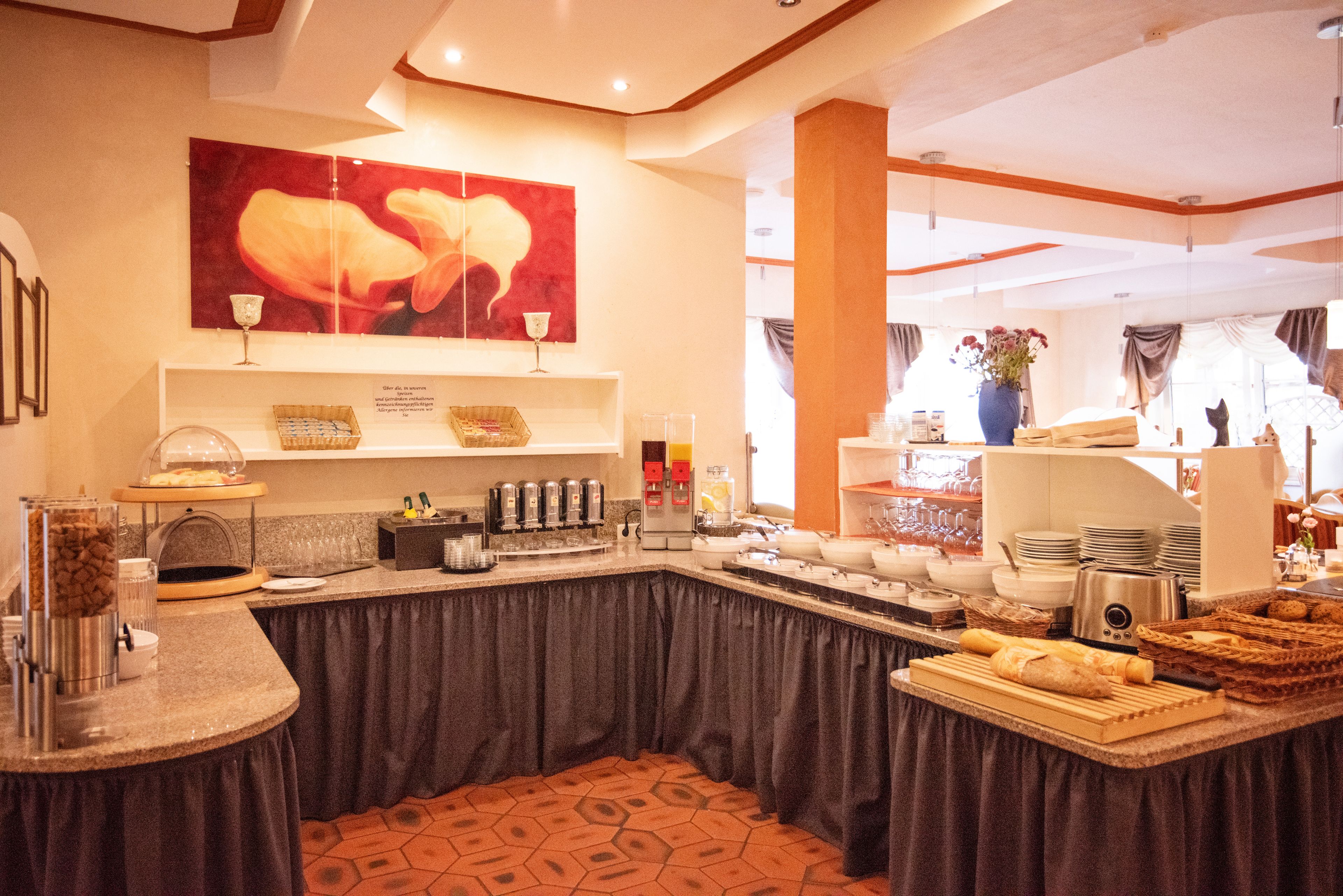 Una mesa de buffet con diversos alimentos, una estación de café y una gran obra de arte floral en la pared.