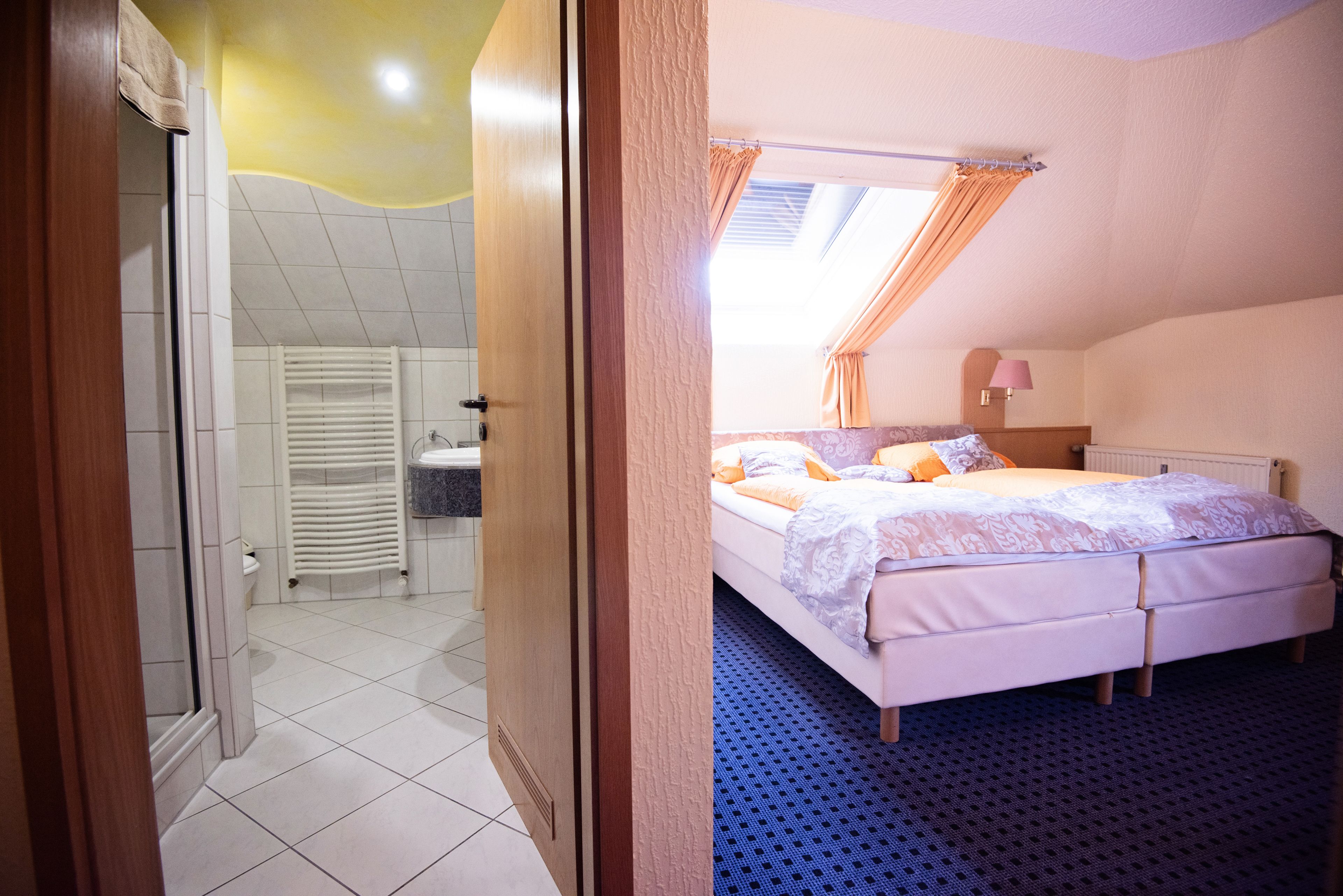 Ein Schlafzimmer mit Bett, einem Fenster mit Vorhängen, einem Badezimmer mit Toilette und Waschbecken sowie einer Duschkabine.