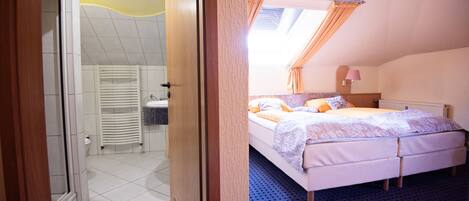 A bedroom with a bed, a window with curtains, a bathroom with a toilet and sink, and a shower area.
