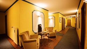 A hotel hallway with yellow walls, a radiator, two armchairs, a round table, and a clock. - Hotel Heideparadies (Soltau)